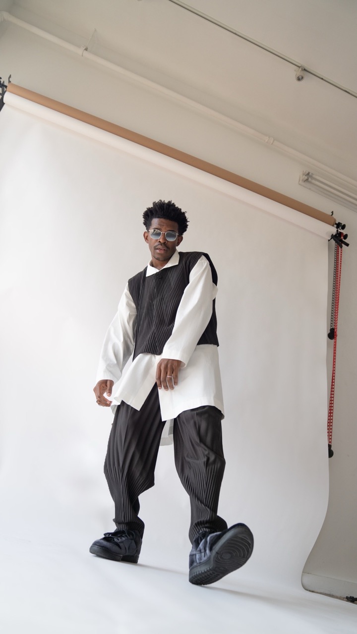 Full-length shot of a young adult male in a white shirt, black vest, black pants, and black shoes, standing in a photo studio.