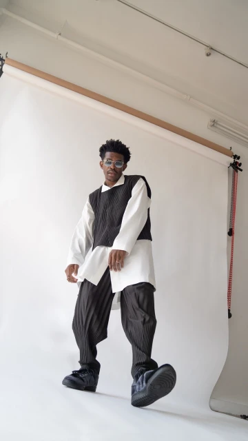 Full-length shot of a young adult male in a white shirt, black vest, black pants, and black shoes, standing in a photo studio.