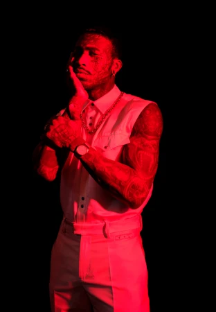 Man wearing a white sleeveless collared shirt and white trousers under dramatic red lighting against a dark background