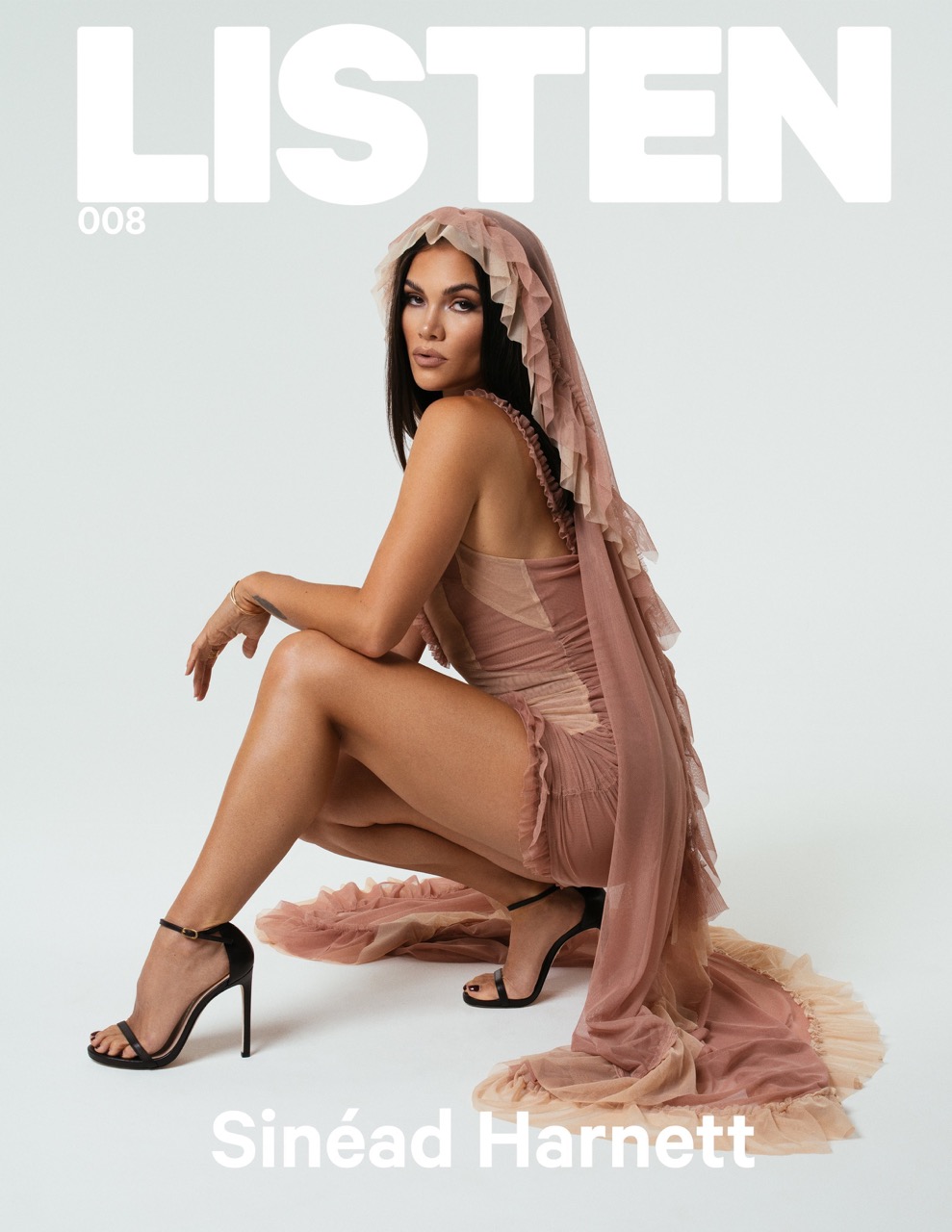 Singer-songwriter Sinéad Harnett poses on a white background wearing a couture gown and black high heels for a fashion magazine cover.