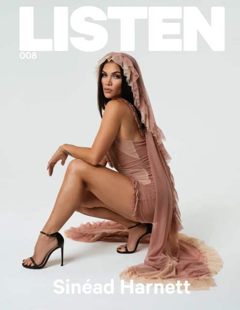 Singer-songwriter Sinéad Harnett poses on a white background wearing a couture gown and black high heels for a fashion magazine cover.