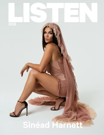 Singer-songwriter Sinéad Harnett poses on a white background wearing a couture gown and black high heels for a fashion magazine cover.