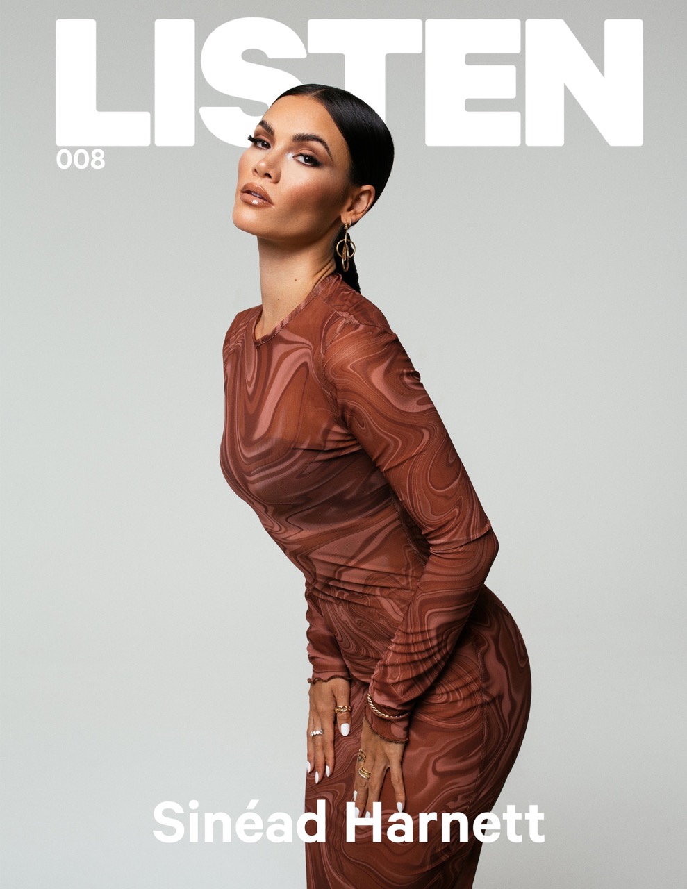 Elegant woman in brown patterned dress poses gracefully against a light gray background, featured on the cover of LISTEN magazine.