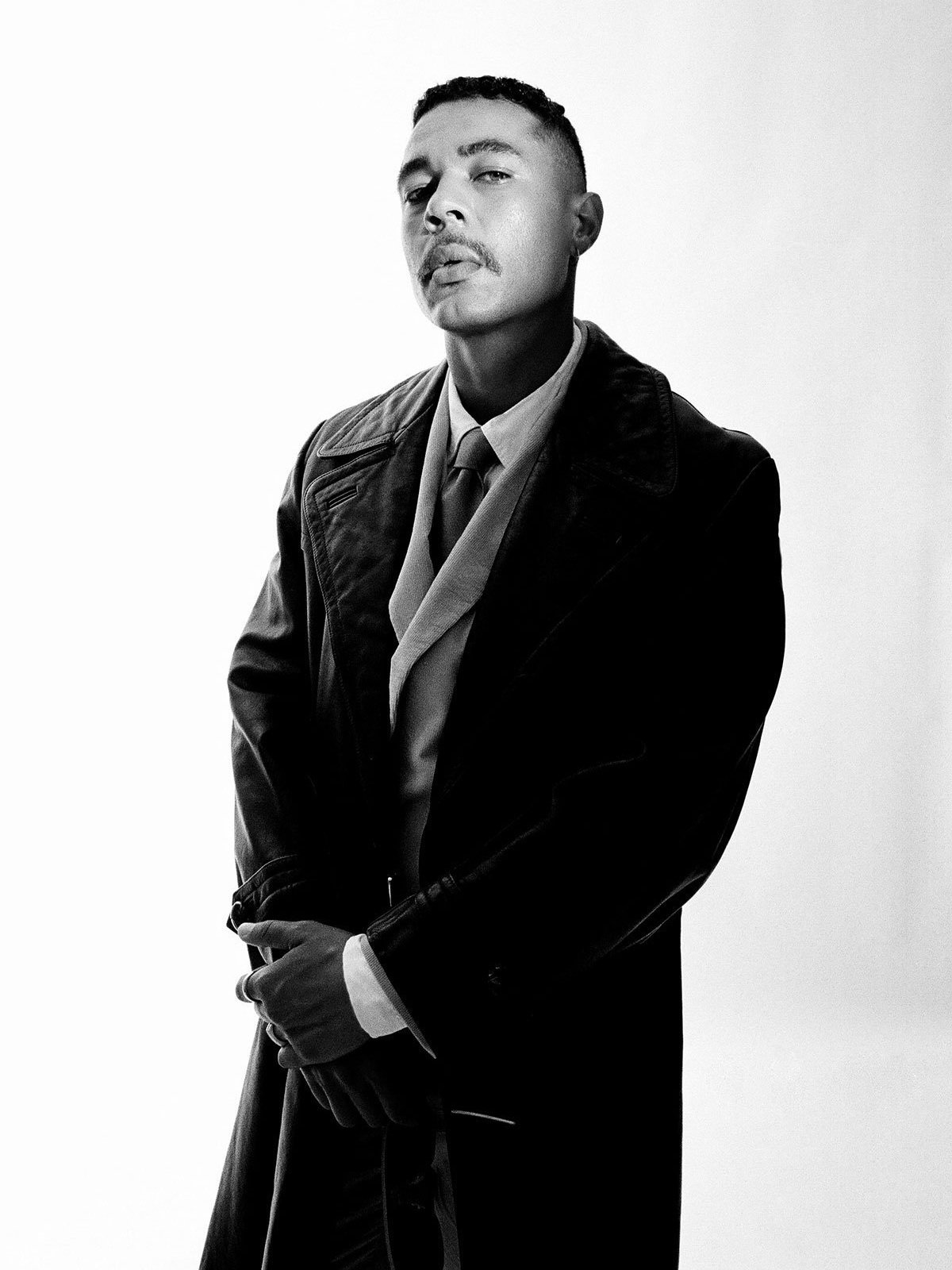 Black and white portrait of a man wearing a dark coat and collared shirt against a white background.