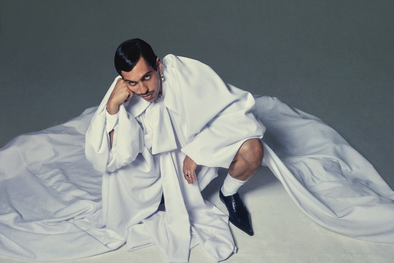 Stylish adult male in dramatic pose with black shoes and white robe on grey background. High-fashion studio portrait.