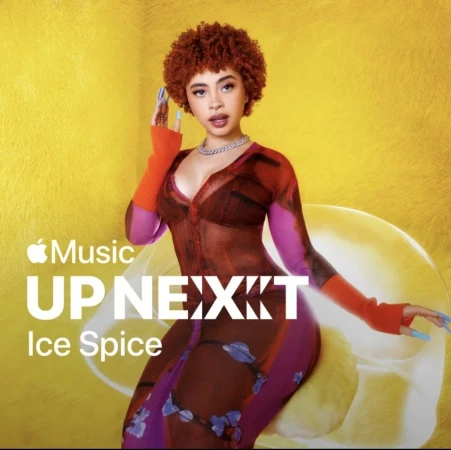 A portrait of rapper Ice Spice, with her signature orange curly hair, wearing a sheer patterned dress against a bright yellow background.