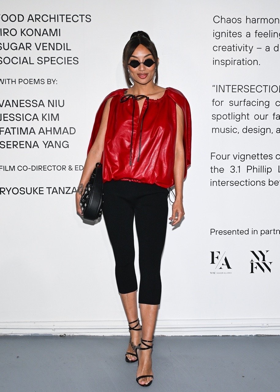 Adult female poses in red top and black leggings with accessories in an indoor setting, fashion runway-inspired against text backdrop.