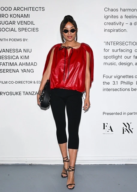 Adult female poses in red top and black leggings with accessories in an indoor setting, fashion runway-inspired against text backdrop.