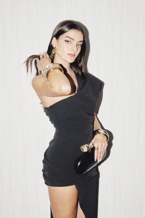 Woman in a black one-shoulder dress holding a black clutch against a textured white backdrop