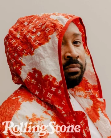 Portrait of a bearded adult male wearing a red and white patterned hooded jacket, with 'Rolling Stone' logo in the lower left corner.