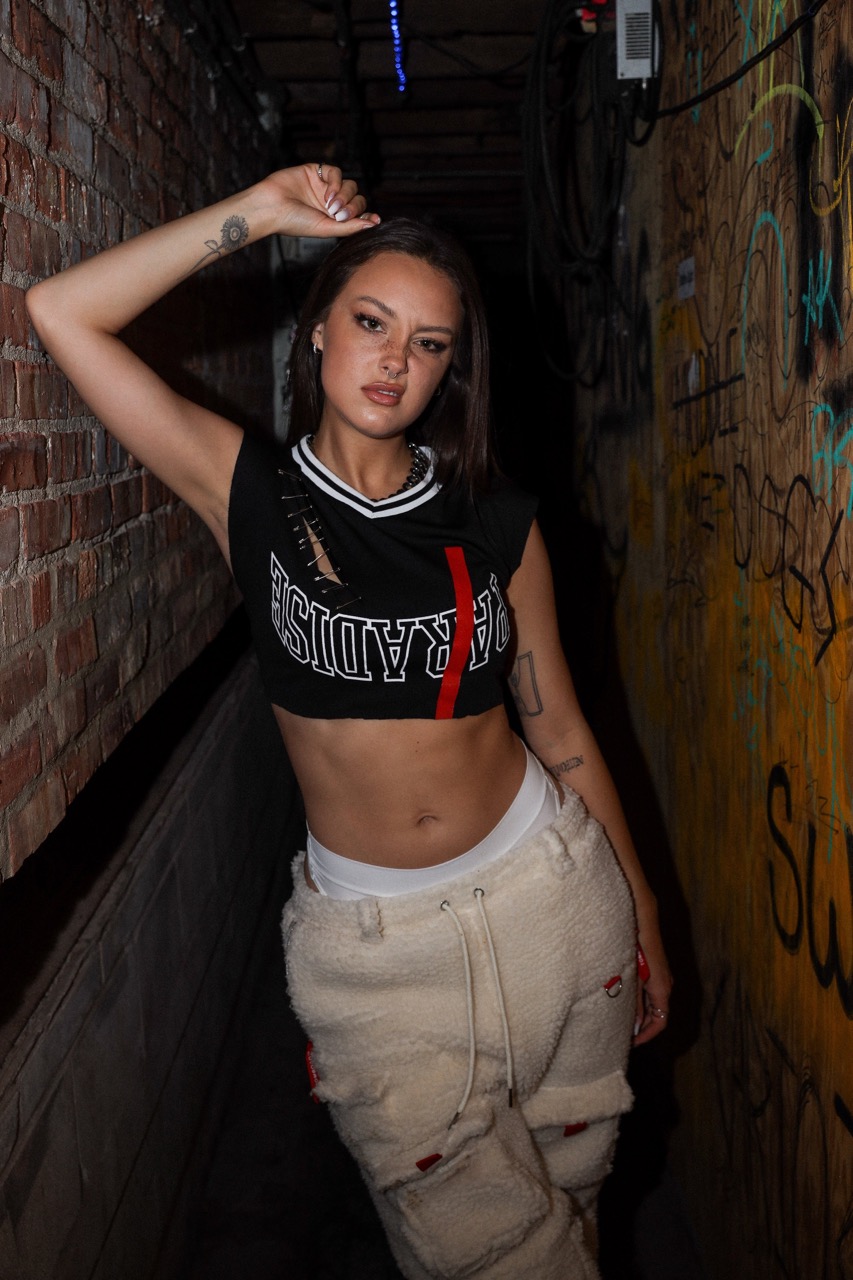 Stylish woman in crop top and cargo pants poses in an urban tunnel setting with graffiti, showcasing streetwear fashion.