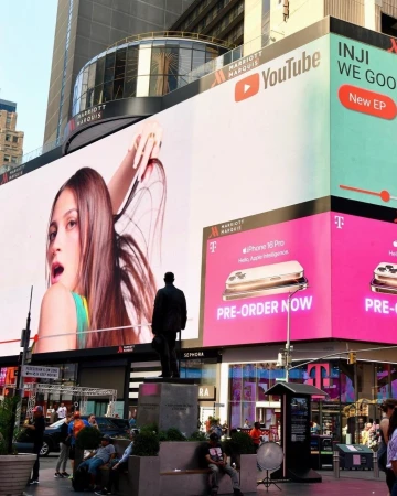 Billboards advertising YouTube, iPhone, and INJI WE GOO on a building in Times Square with a statue and people in the foreground.