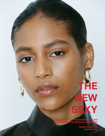 Close-up portrait of a woman wearing gold hoop earrings and a dark high-neck garment against a plain white background.