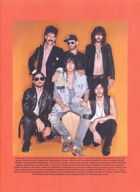 Group portrait of six young adult men wearing denim and leather jackets, button-down shirts, and jeans, posed on an orange background.