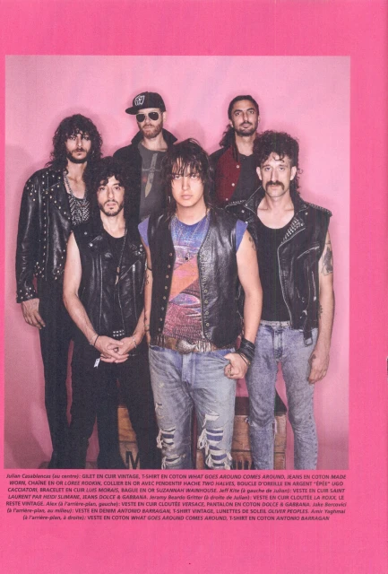 Group of six people in leather jackets and jeans posing against a pink backdrop in a full shot, displaying alternative fashion.