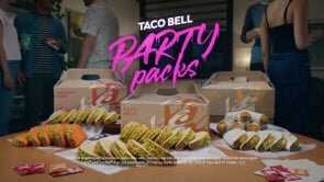 A table laden with Taco Bell party packs, surrounded by a blurred group of people, hints at a casual gathering and fast-food catering.