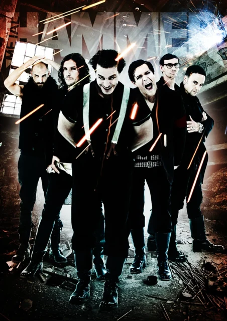 Group of six people in black clothing stand in an industrial setting with beams of light, evoking a metal music vibe.