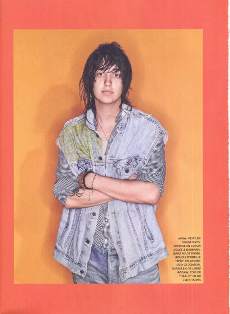 Person wearing denim vest and jeans stands in front of orange background in editorial fashion shot with natural light. 
