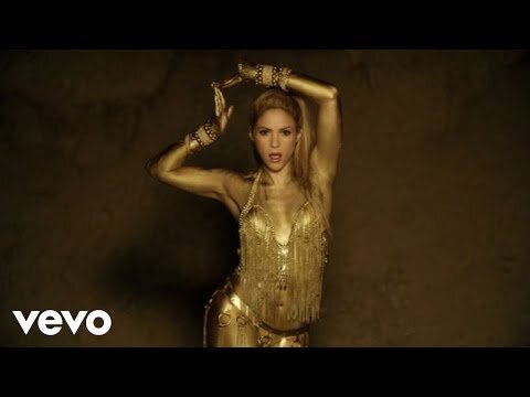 A fair-skinned adult female with blonde hair is covered in gold paint, wearing a matching outfit while posing with her hands above her head.