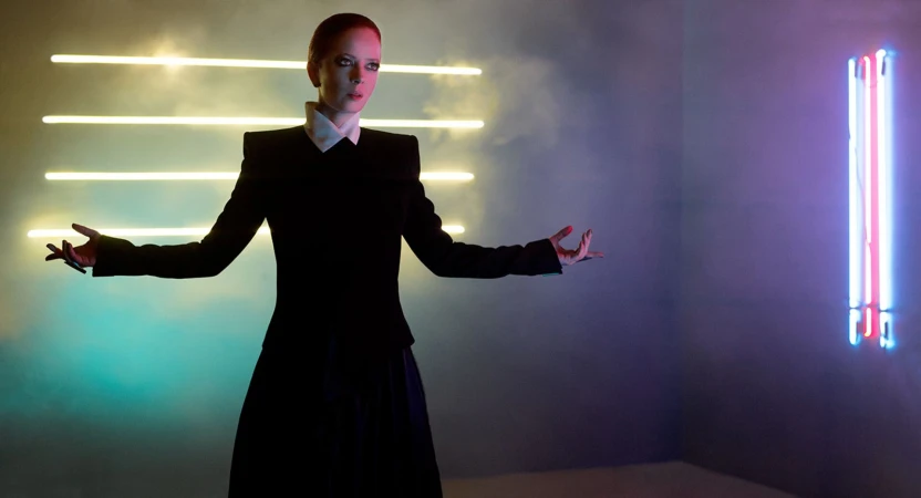 Woman in black dress poses with arms outstretched in a room with neon lights creating a futuristic, fashion-forward and stylized aesthetic.