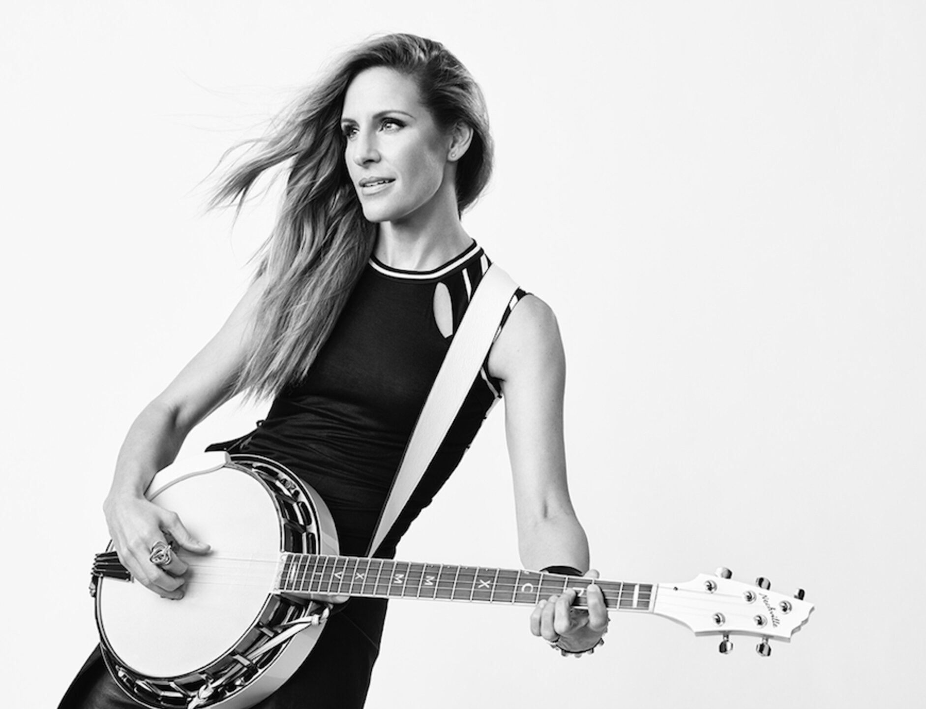 Black and white portrait of an adult woman playing a banjo with a white background, looking to the side with long, wavy hair.