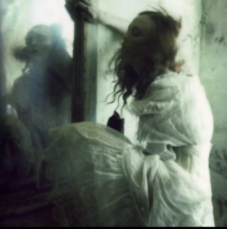 Artistic, blurred image of a woman in a white dress gazing into a vintage mirror with visible wall texture in a shadowy indoor space.