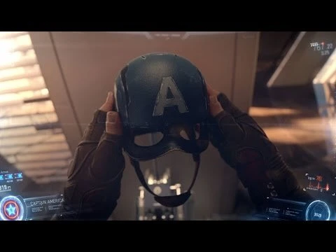 Close-up shot of hands holding a Captain America helmet with a large 'A' on it, futuristic interior background with glowing interface elements.