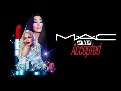 MAC Cosmetics Challenge Accepted campaign featuring two women, Cher and Saweetie, next to a large red lipstick and makeup brushes on a black backdrop.