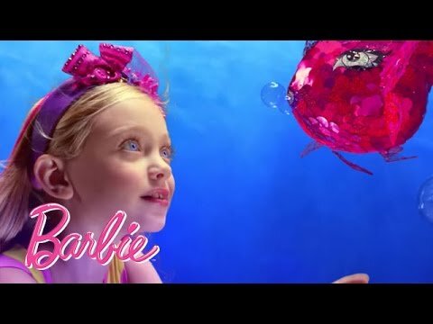 A young girl wearing a purple bow and a pink fish art installation appear together in front of an ocean blue backdrop.