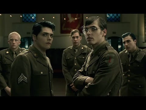 Group of five men in olive green military uniforms with crew cuts in dimly lit indoor setting. Old fashioned war-themed visual.