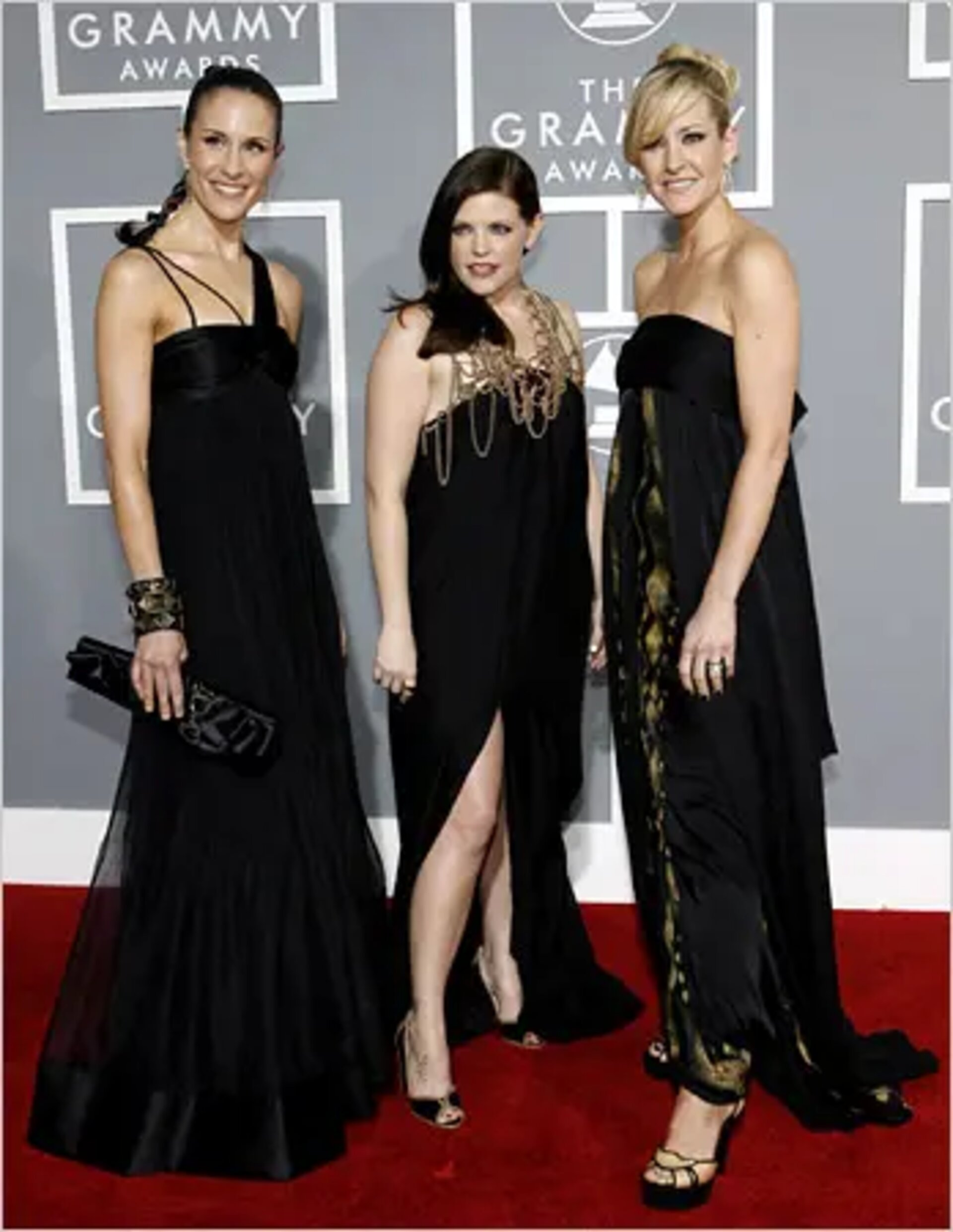 Three women on a red carpet wearing black gowns at the Grammy Awards, captured in a medium shot highlighting their elegant attire and style.