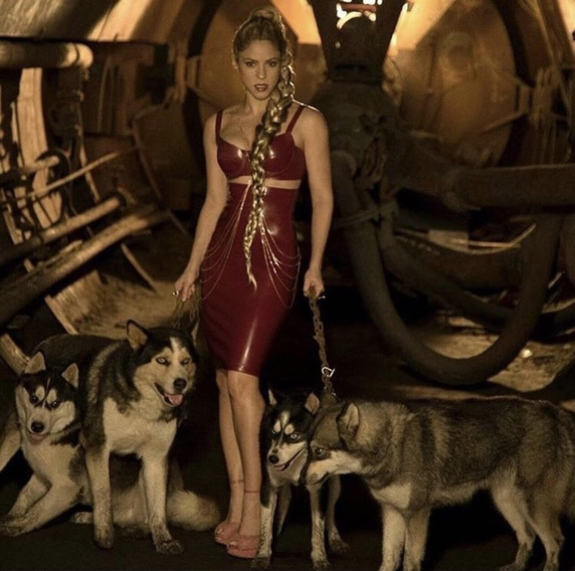 Adult woman in red latex dress poses with four huskies in an industrial setting, creating a dark and edgy fashion statement.