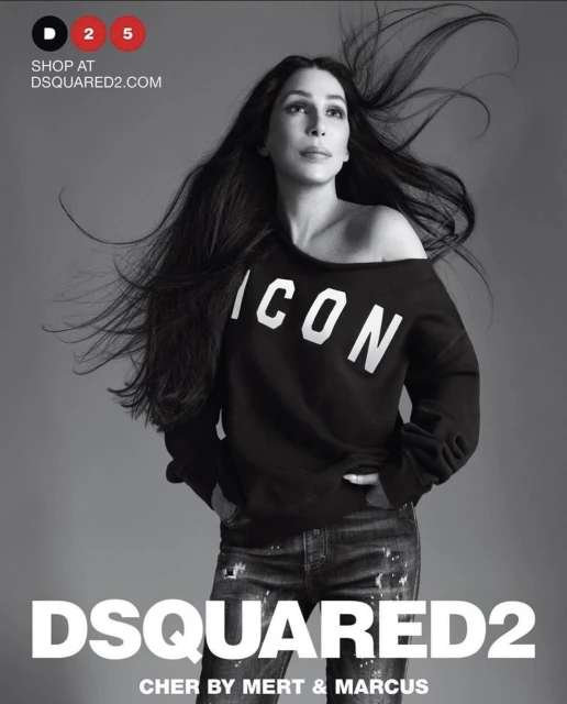 A woman with long, dark hair poses in a black, off-the-shoulder 'ICON' sweatshirt and embellished jeans against a gray background for a Dsquared2 ad.