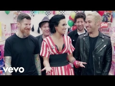 Group shot featuring Demi Lovato and members of Fall Out Boy in a brightly colored candy store setting for a music video.