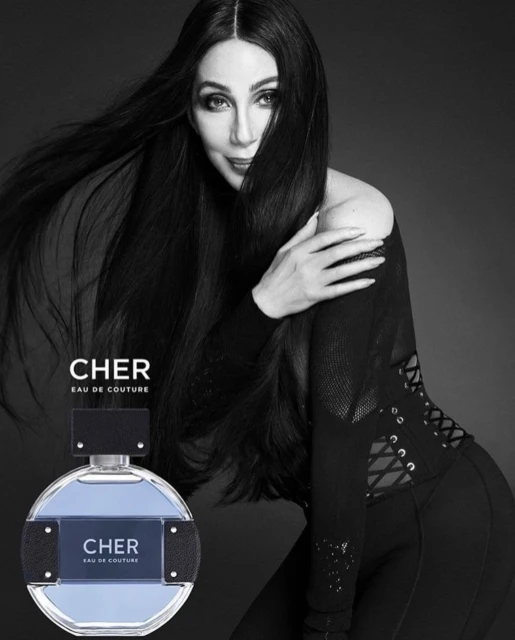 Black and white photo of singer Cher promoting her fragrance, Eau de Couture. The perfume bottle is in the foreground.