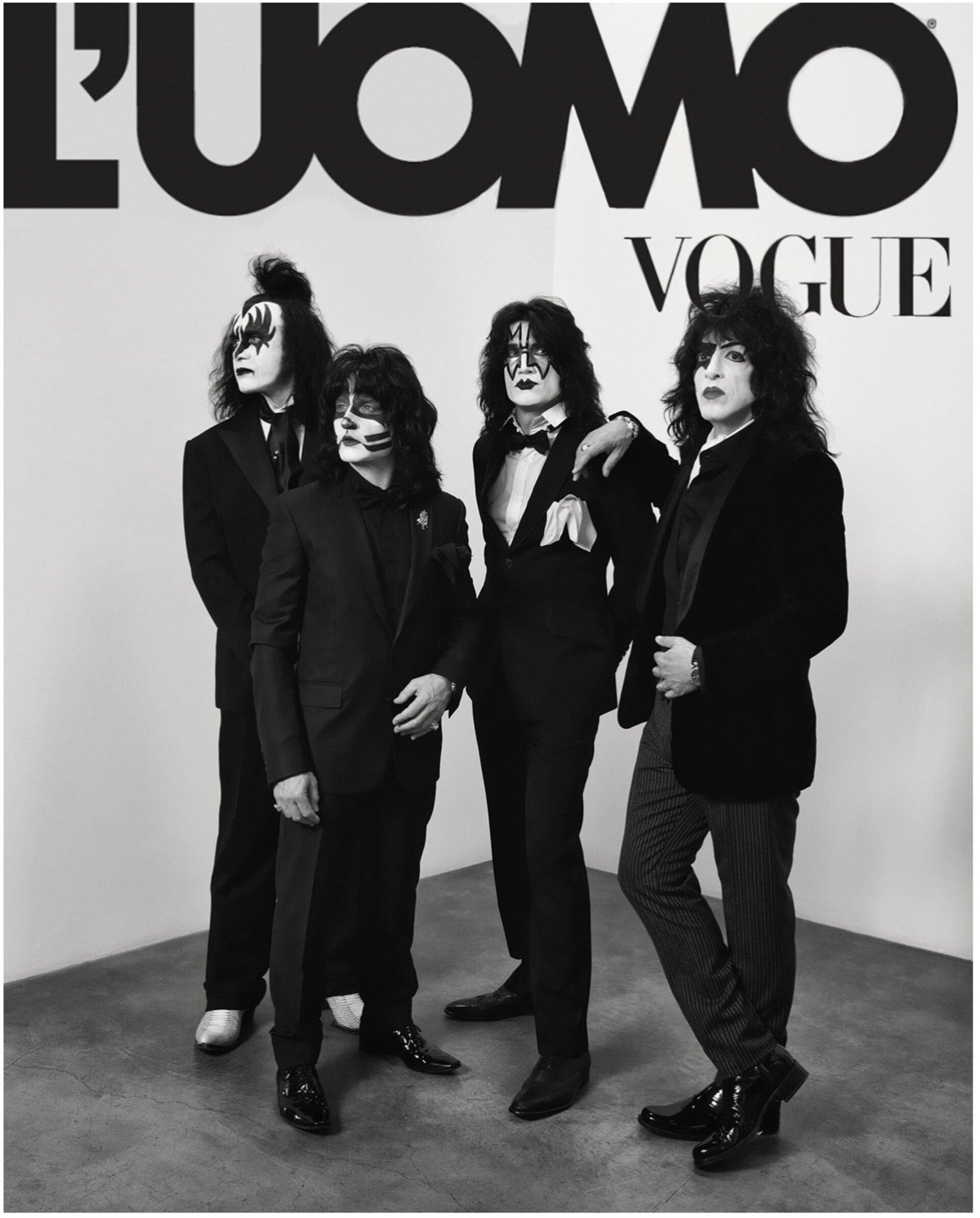 Four people in black suits with theatrical makeup pose in a studio, reminiscent of the rock band KISS, for L'Uomo Vogue.