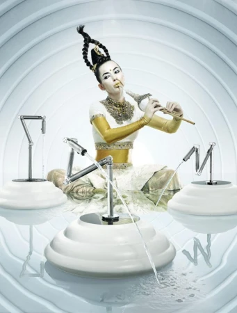 Asian woman with elaborate updo and makeup playing flute, seated in an artistic set with water features in an indoor environment.