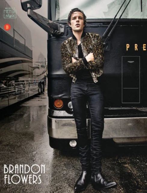 Brandon Flowers, the lead singer of The Killers, leans against a black tour bus wearing a leopard print jacket and black jeans.
