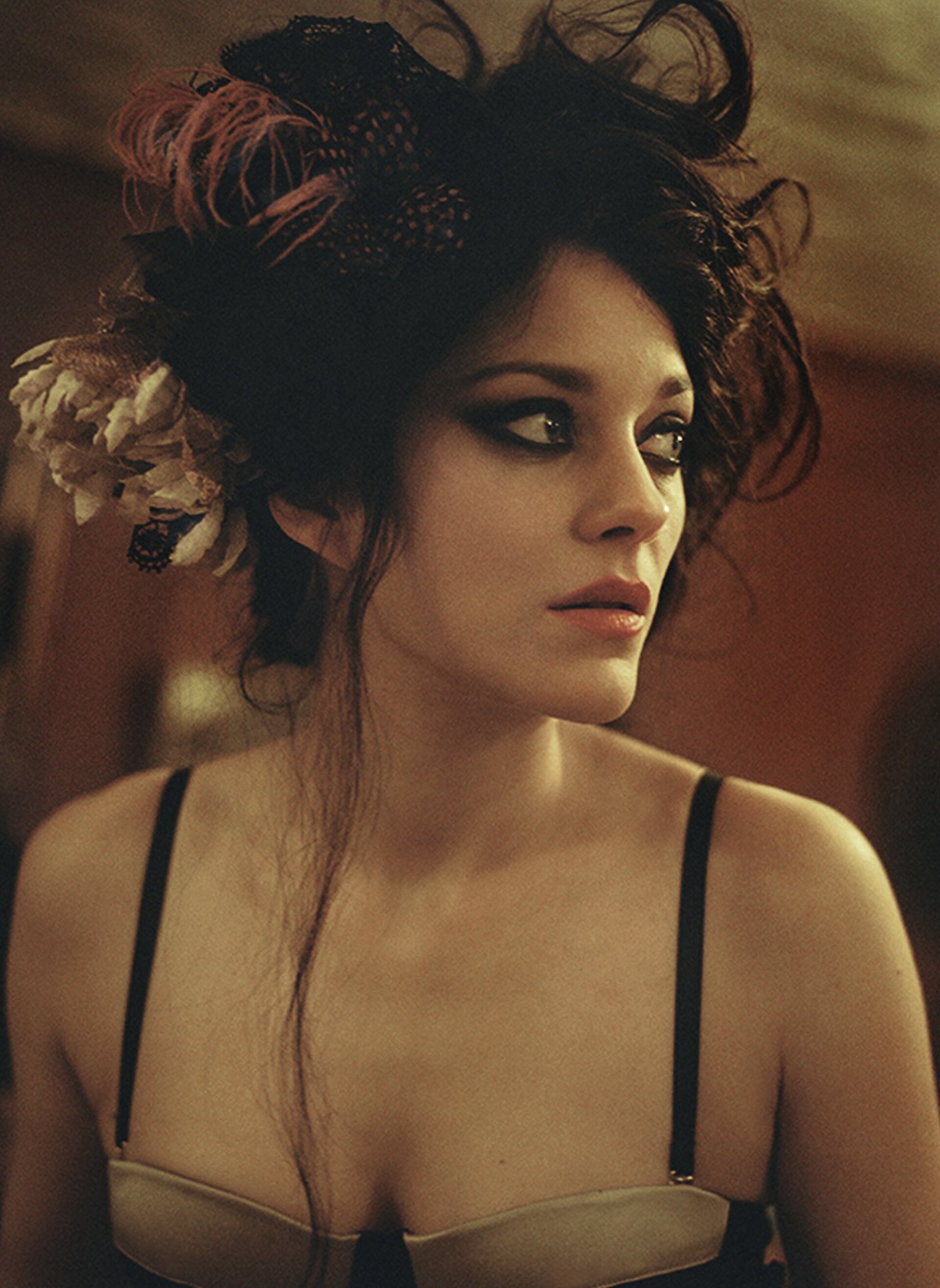 Glamorous portrait of a woman with dark eye makeup, a floral hair accessory, and a strapless top against a muted red background.