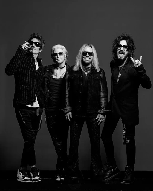 Black and white studio shot of four adult males in dark clothing and sunglasses, in a vertical portrait-style composition.