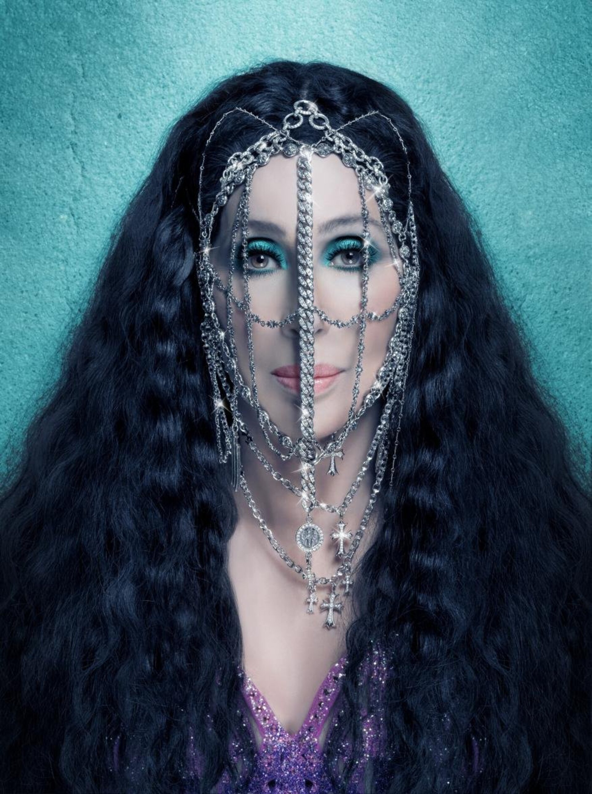 A portrait of Cher wearing a jeweled headpiece and purple sequin top against a textured teal background in a studio setting.