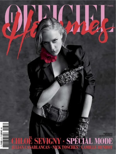 Chloë Sevigny poses on a magazine cover wearing a black blazer, jeans, and decorative gloves against a grey background.