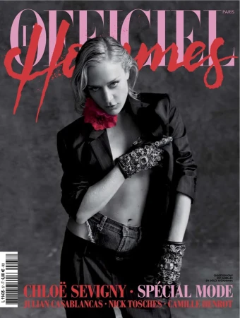 Chloë Sevigny poses on a magazine cover wearing a black blazer, jeans, and decorative gloves against a grey background.