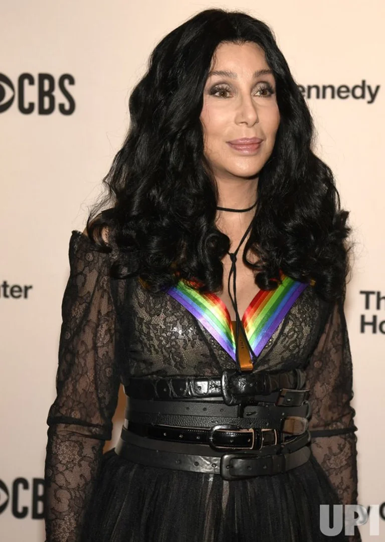 Headshot of Cher at the Kennedy Center Honors wearing a black lace dress, wide black belts, and a colorful necklace.