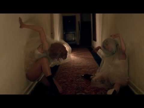 Two individuals covered in clear plastic, posing artistically in an indoor hallway with muted colors, creating an eerie and captivating scene.