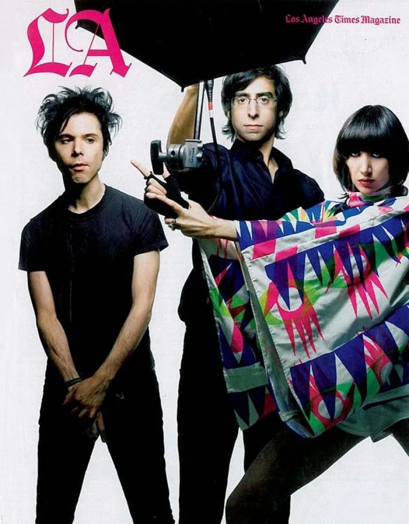 Magazine cover featuring three musicians, one holding an umbrella and another wearing a patterned shawl, against a white background.