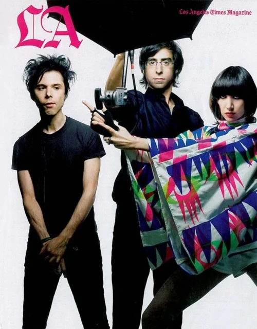Magazine cover featuring three musicians, one holding an umbrella and another wearing a patterned shawl, against a white background.