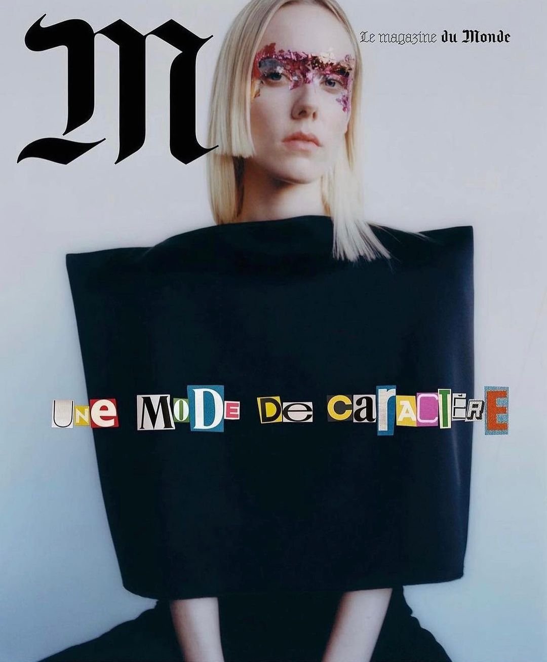 Fashion editorial featuring a woman with blonde hair, wearing a black dress and colorful eye makeup, posing against a light background.