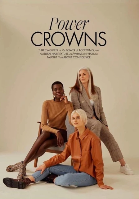 Three diverse women pose in a studio with warm lighting for a fashion editorial, each wearing stylish clothing, promoting natural hair texture.