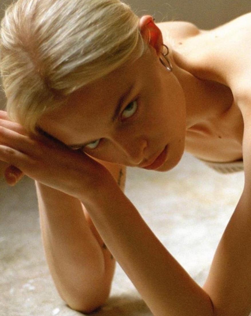 Close-up studio shot of a fair-skinned young woman with blonde hair looking at the camera with green eyes, leaning on her arms.